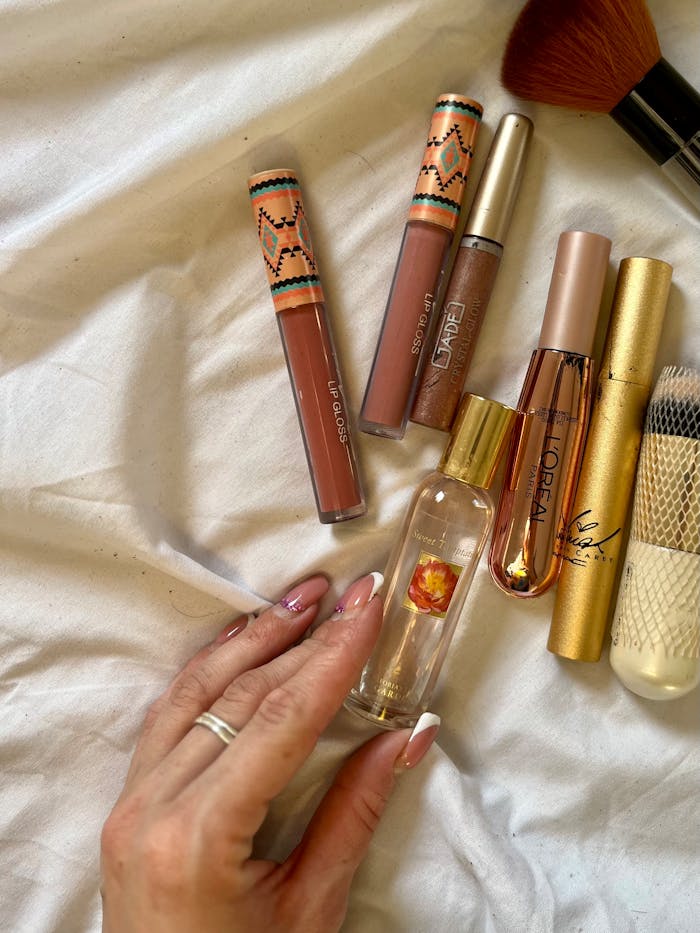 services-02 A stylish flat lay of cosmetics including lip gloss, mascara, and a hand holding a perfume bottle.